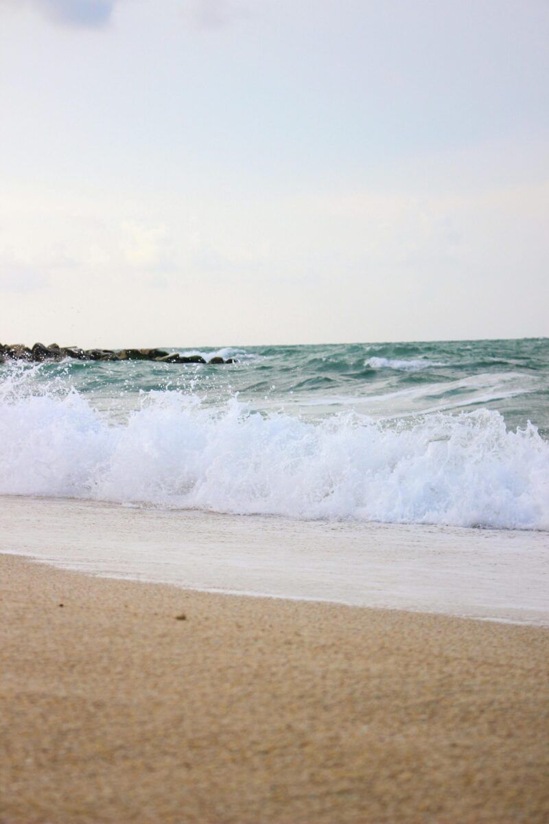 Peaceful sandy beach with foamy waves under a clear sky, perfect for relaxation.